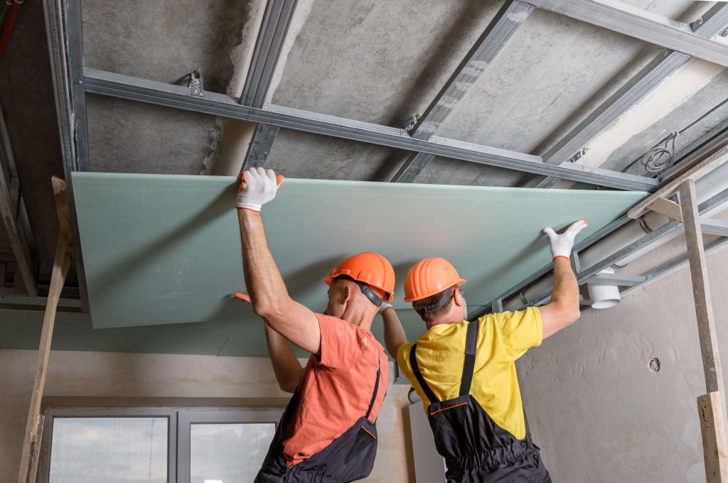 Gyprocker installing a plasterboard on metal ceiling framework